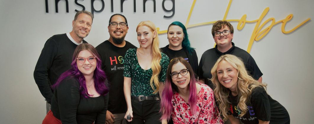 A group of eight people smiling in front of a wall with the words "Inspiring Hope" in large, modern font.