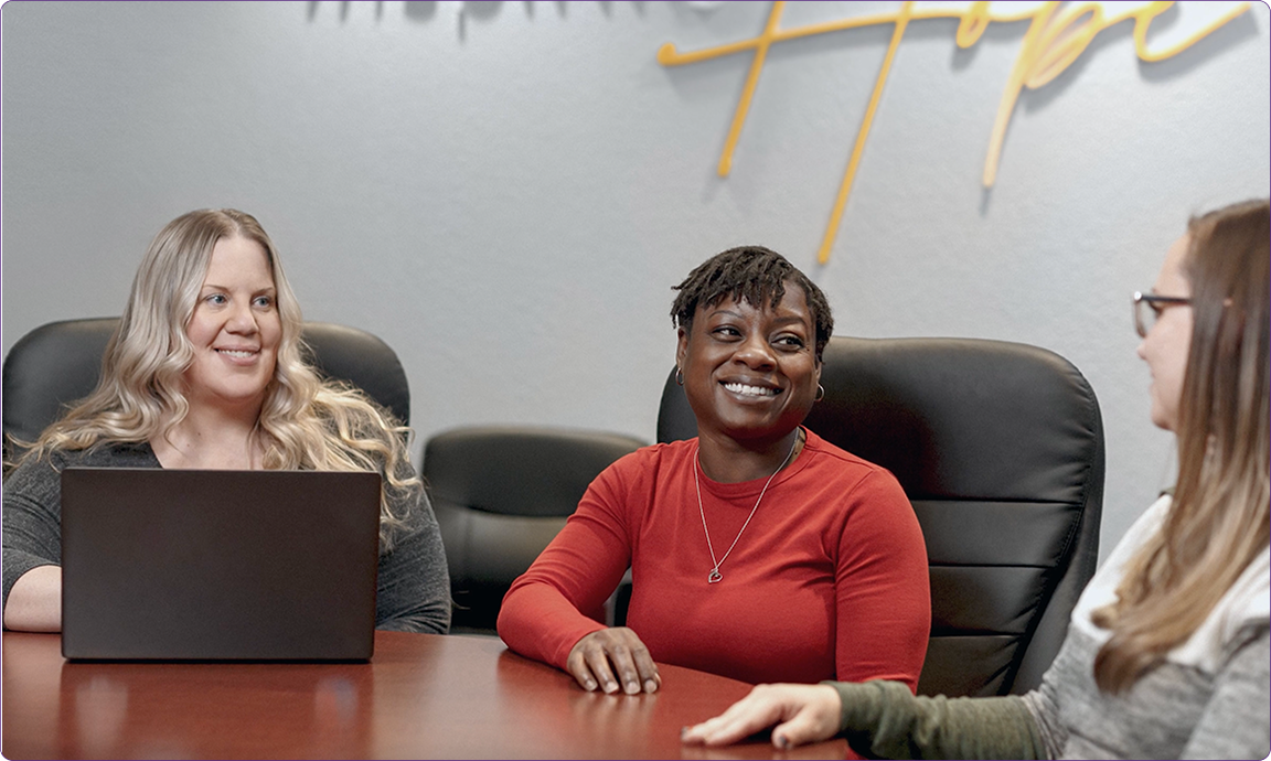 Three people sitting around a table, engaged in conversation, with a laptop and "Hope" written in the background.