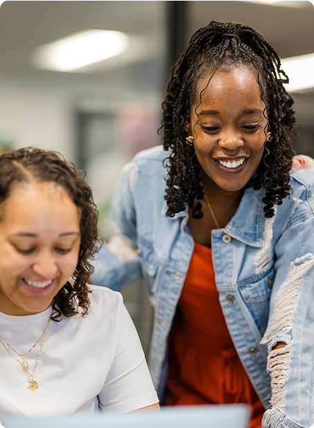 Two people are happily collaborating in an office setting, focusing on shared work. The atmosphere appears friendly and engaging.