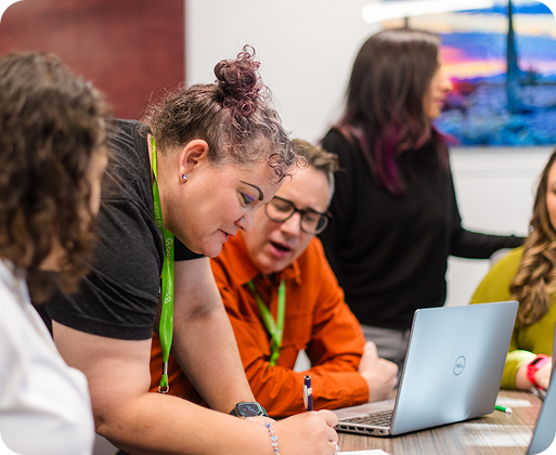 A group of five people collaborate at a table with a laptop, focusing on a task, in a modern indoor setting.