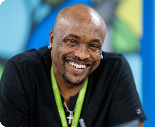 A person wearing a green lanyard smiles warmly at the camera, with a colorful, abstract background enhancing the cheerful atmosphere.